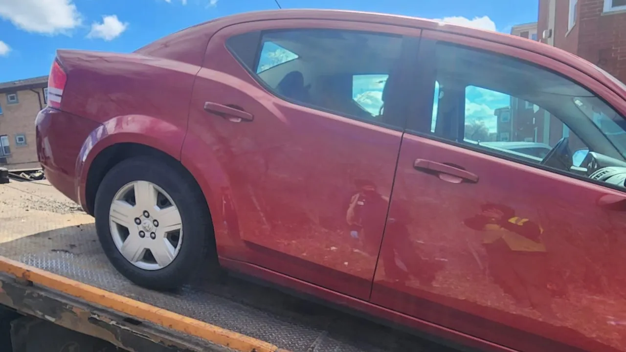 Red sedan loaded on a flatbed after a pickup.