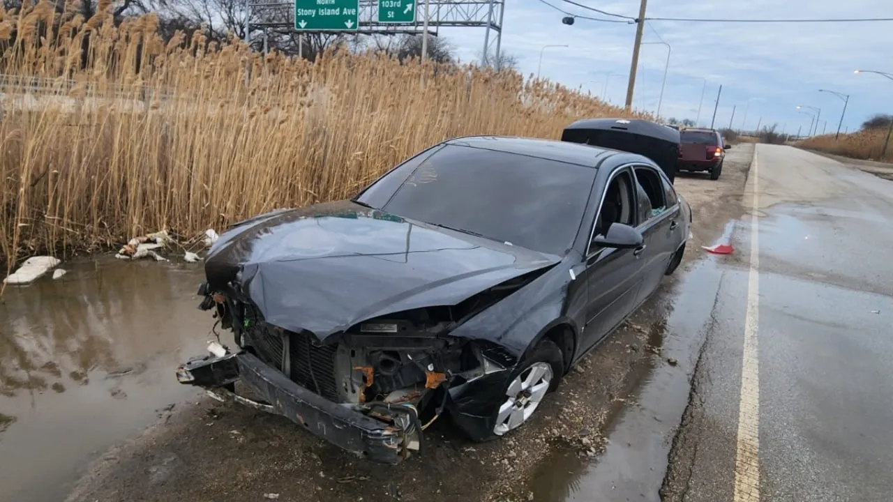 Black sedan with its front end torn off, stopped on a road shoulder.